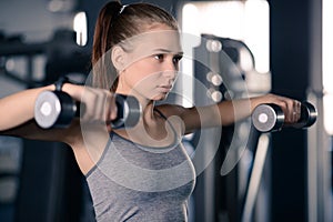 Attractive Young Sports Woman Lifting Dumbbells in the Gym. Fitness and Healthy Lifestyle.