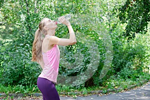 Attractive young sportwoman finished her work out and now drinking water and smiling in the park