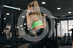 Attractive young sporty woman is working out in gym. Cross fit training. Muscular woman is squatting with barbell