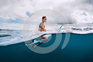 Attractive young surf girl sit at surfboard in ocean