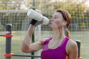 Attractive young swart woman in bright sportswear drinks water during fitness on outdoors sportsground. Active lifestyle woman hyd