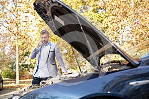 Attractive young upset man making a call while his car broke down