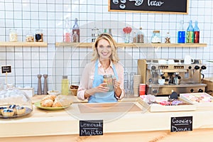 attractive young waitress holding glass jar with lemonade and smiling