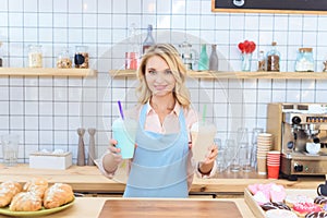 attractive young waitress holding milkshakes in plastic cups and smiling