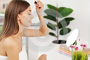 Attractive young woman applying serum on face with pipette