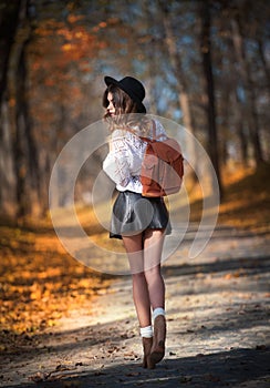 Attractive young woman in an autumnal shot outdoors. Beautiful fashionable school girl posing in park with faded leaves around