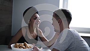 Attractive young woman with bath towel on her head is sitting with her boyfriend or husband on the kitchen table. Having