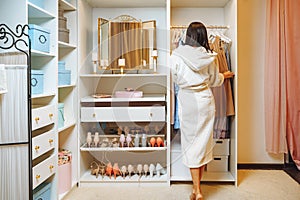 Attractive young woman in bathrobe choosing a dress in dressing room at home