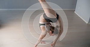 Attractive young woman bends over backwards and performs various yoga and gymnastic exercises on the floor, person makes