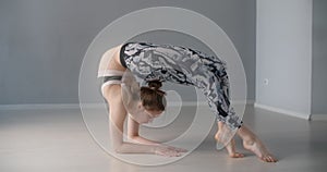 Attractive young woman bends over forward and performs various yoga and gymnastic exercises on the floor, person makes