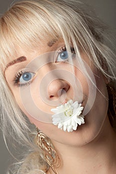 Attractive young woman with big blue eyes and a chrysanthemum in her mouth