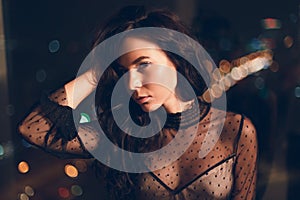 Attractive young woman in black cocktail dress in front of window at night