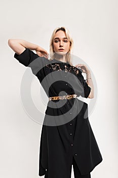 Attractive young woman blond with sexy lips in black long fashionable dress with trendy leopard strap poses near white vintage