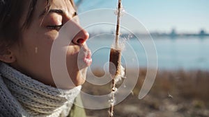 Attractive young woman blowing on dry cone of reeds.