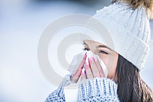 Attractive young woman blowing her nose with a tissue in winter