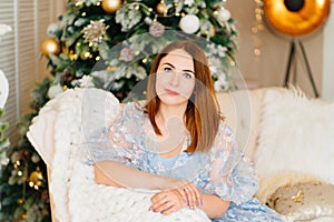 an attractive young woman in a blue dress on the couch by the Christmas tree