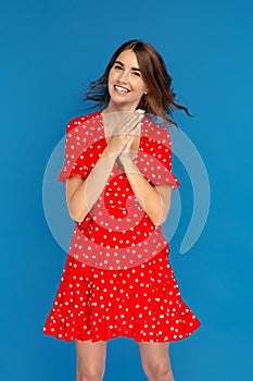 Attractive young woman with bright smile in red dress feeling happy over blue background.