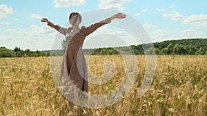 attractive young woman in brown dress walks along yellow field against blue sky with clouds. beautiful beauty lady spin