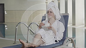 Attractive young woman with brown eyes drinking tea or coffee and smiling. Portrait of positive rich client resting on