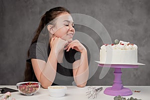 Attractive young woman brunette confectioner presents a white cake with small red flowers of a food rose.