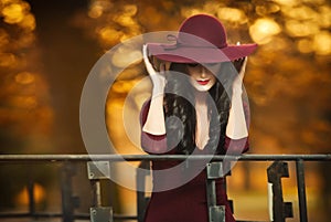 Attractive young woman with burgundy colored large hat in autumnal fashion shot. Beautiful mysterious lady covering the face