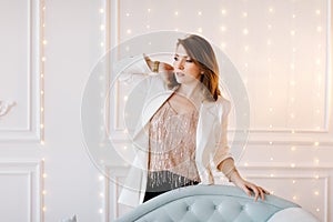 Attractive young woman in a business suit with white jacket, black pants and high heels near a blue classic sofa. White background