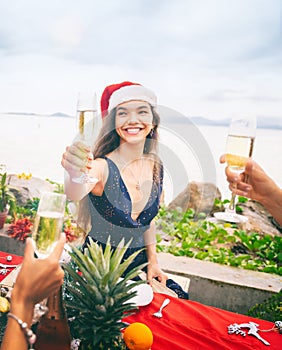 Attractive young woman celebrating Christmas in Santa Claus hat and New Year on a tropical beach, holding champagne glasses in