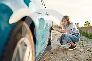 Attractive young woman checking air pressure of car tire on local road side while traveling, Girl having troubles with