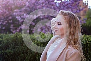 Attractive young woman with closed eyes and red hair in blooming spring park. Cherry blossom tree background. Side view