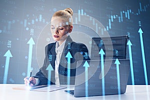 Attractive young woman at desk with laptop and growing blue vertical arrows and candlestick forex chart on blurry index grid