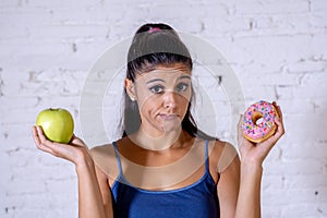 Attractive young woman on a diet deciding between an apple and a doughnut