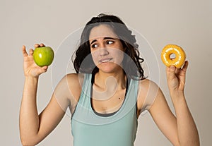 Attractive young woman on a diet deciding between an apple and a doughnut