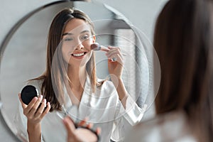 Attractive Young Woman Doing Daily Makeup While Standing Near Mirror In Bathroom