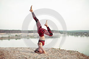 An attractive young woman doing a yoga pose for balance and stretching near the lake high in the mountains