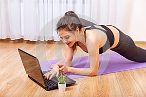 Attractive young woman doing yoga and stretching online at home.