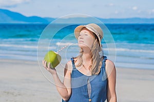 Attractive young woman drinking coconut water on the beach