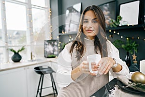 Attractive young woman drinks tea in the kitchen for Christmas