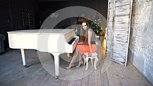 Attractive young woman in evening dress sitting at the white grand piano