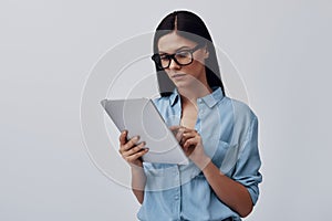 Attractive young woman in eyewear using digital tablet while standing against grey background