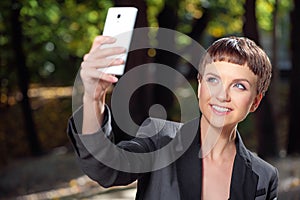 Attractive young woman in formalwear taking photo with her cellphone in park