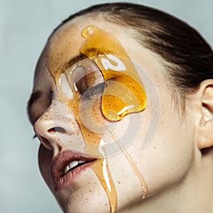 Attractive young woman with freckles making honey homemade mask for skincare posing with closed eyes