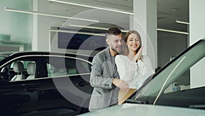 Attractive young woman is getting new car from her boyfriend, he is closing her eyes and leading her to auto in motor