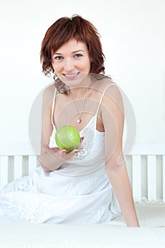 Attractive young woman with an green apple at bed