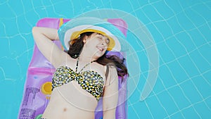 An attractive young woman in a hat is floating on an inflatable mattress in the pool. Ideal vacation concept