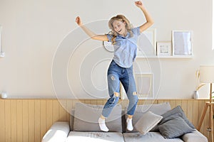 Attractive young woman is having fun at home. Girl is jumping and dancing on sofa