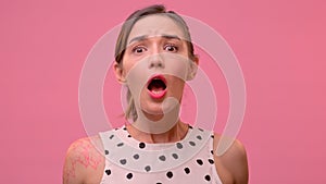 Attractive young woman having stunned and shocked look on a pink background.