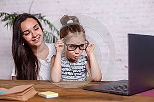 Attractive young woman and her little cute daughter are sitting at the table and having fun while doing homework