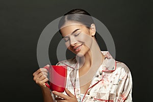 Attractive young woman holding coffee mug on black background. Coffee lover