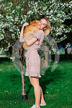 Attractive young woman holding dog spitz outside and smiling at camera, walking in the park