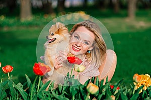 Attractive young woman holding dog spitz outside and smiling at camera, walking in the park